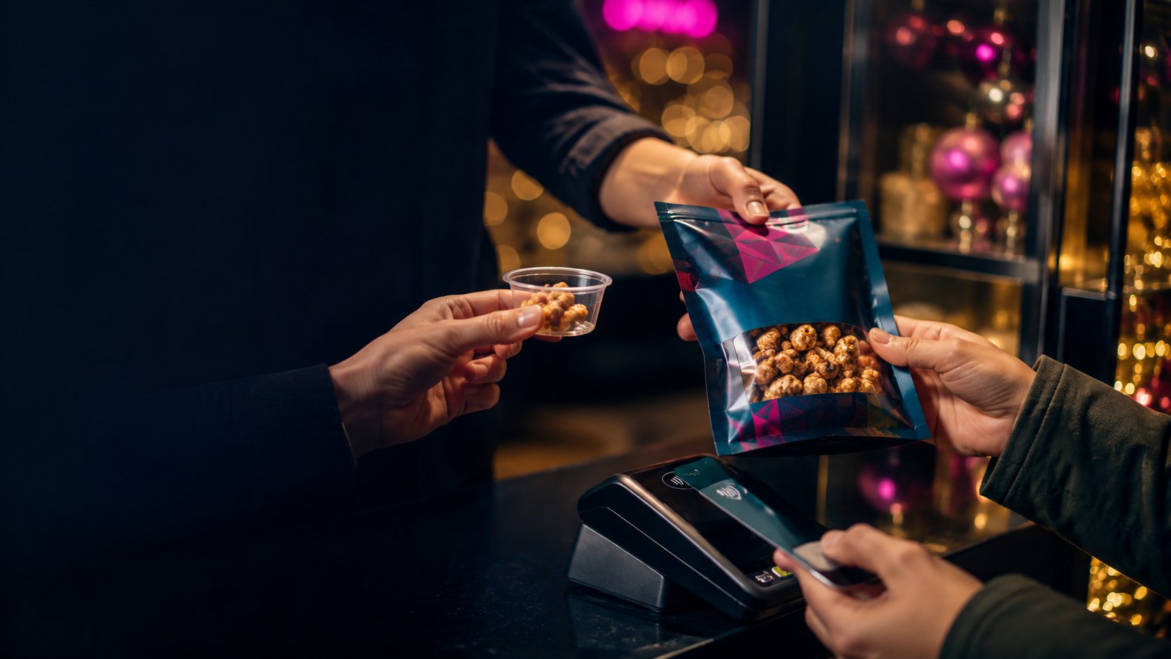 A free sample cup offered in one hand while a customer pays for a full-size bag